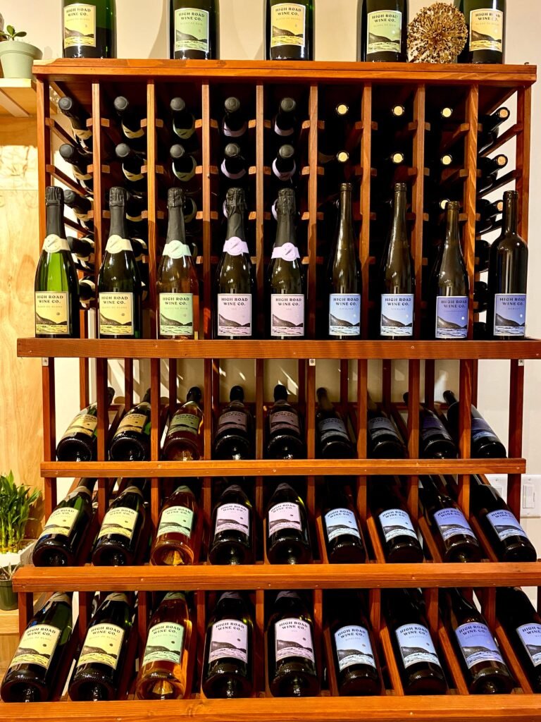 High Road Wine Co. bottles of sparkling and still wine displayed on a wooden wine shelf in the tasting room